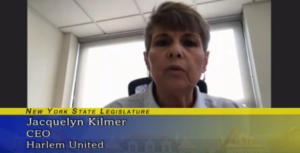 Jacqui Kilmer speaking to the camera. A blue and gold graphic under her face says "New York State Legislature; Jacqui Kilmer; CEO; Harlem United"